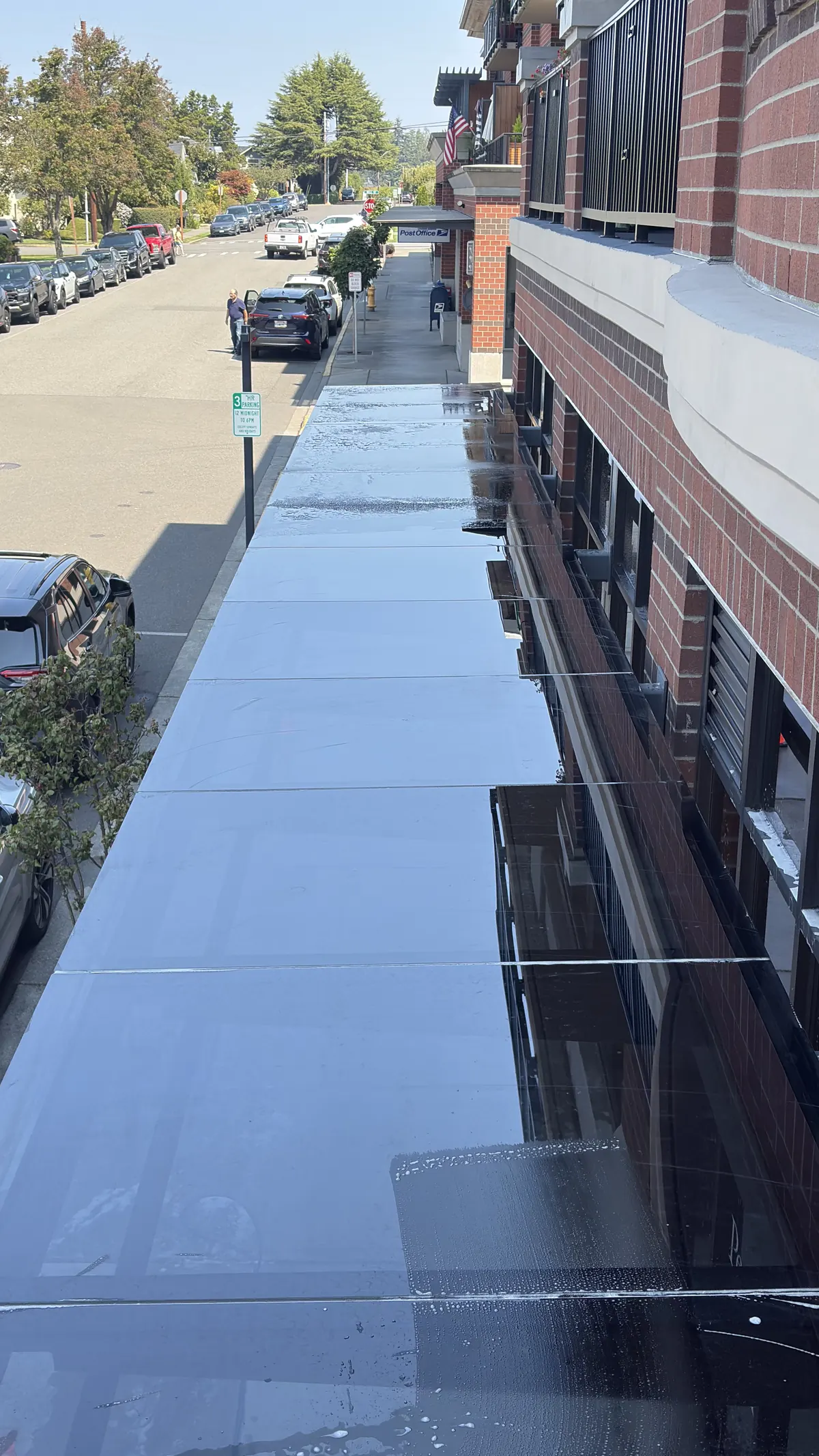 Glass entry canopy on a brick building, wet from cleaning, with the street reflected in the glass