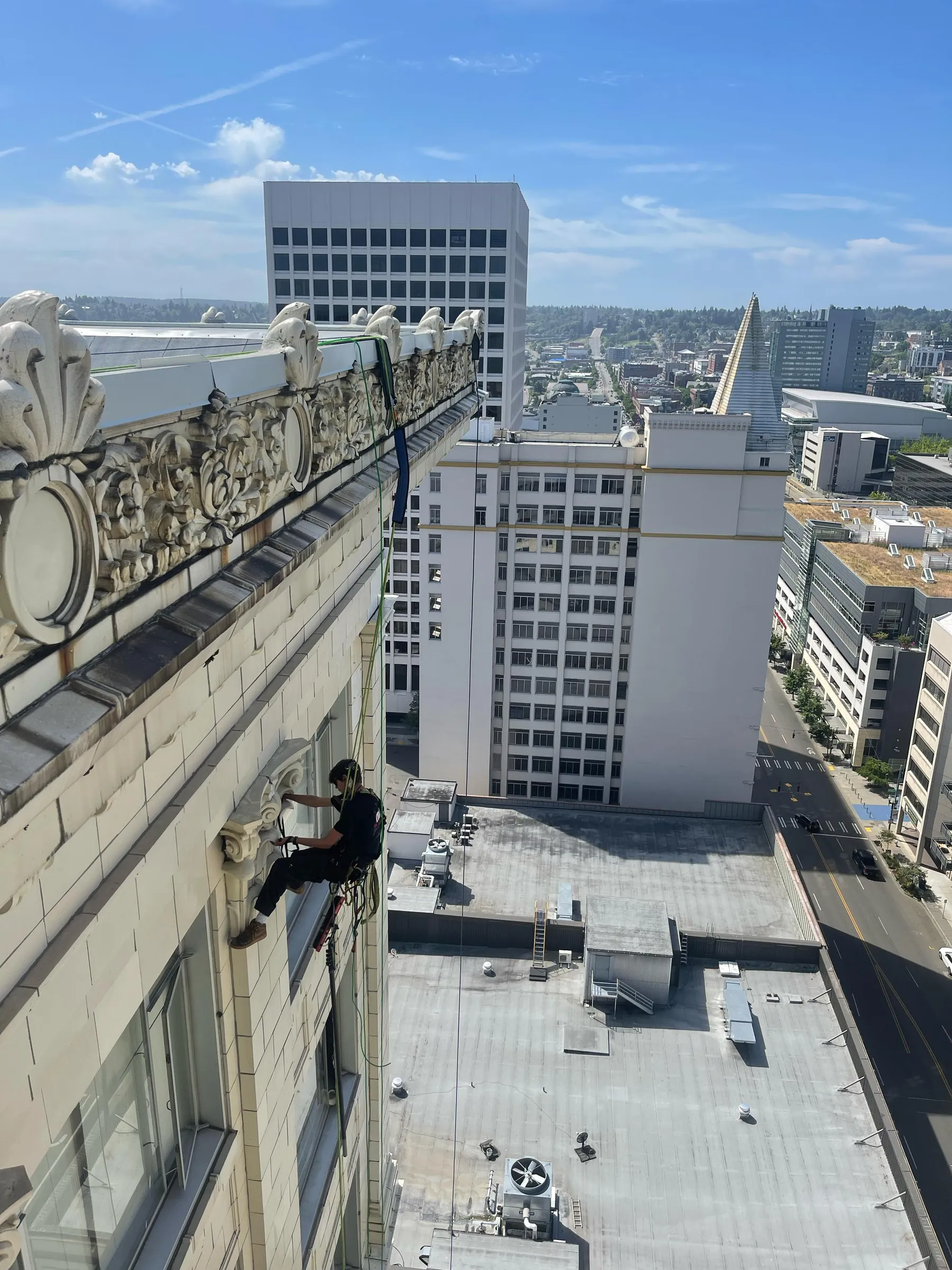 Rope access technician cleaning windows past a stone cornice on an older building