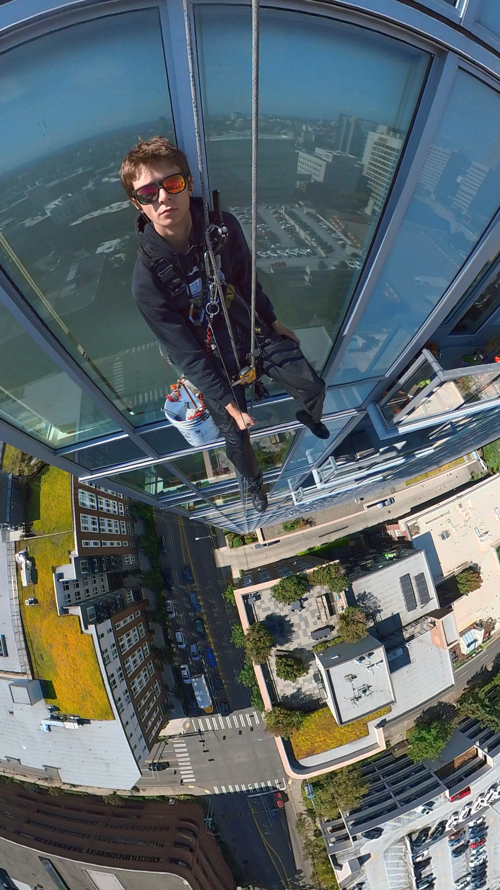 Rope access technician high on a glass building facade, with the city below
