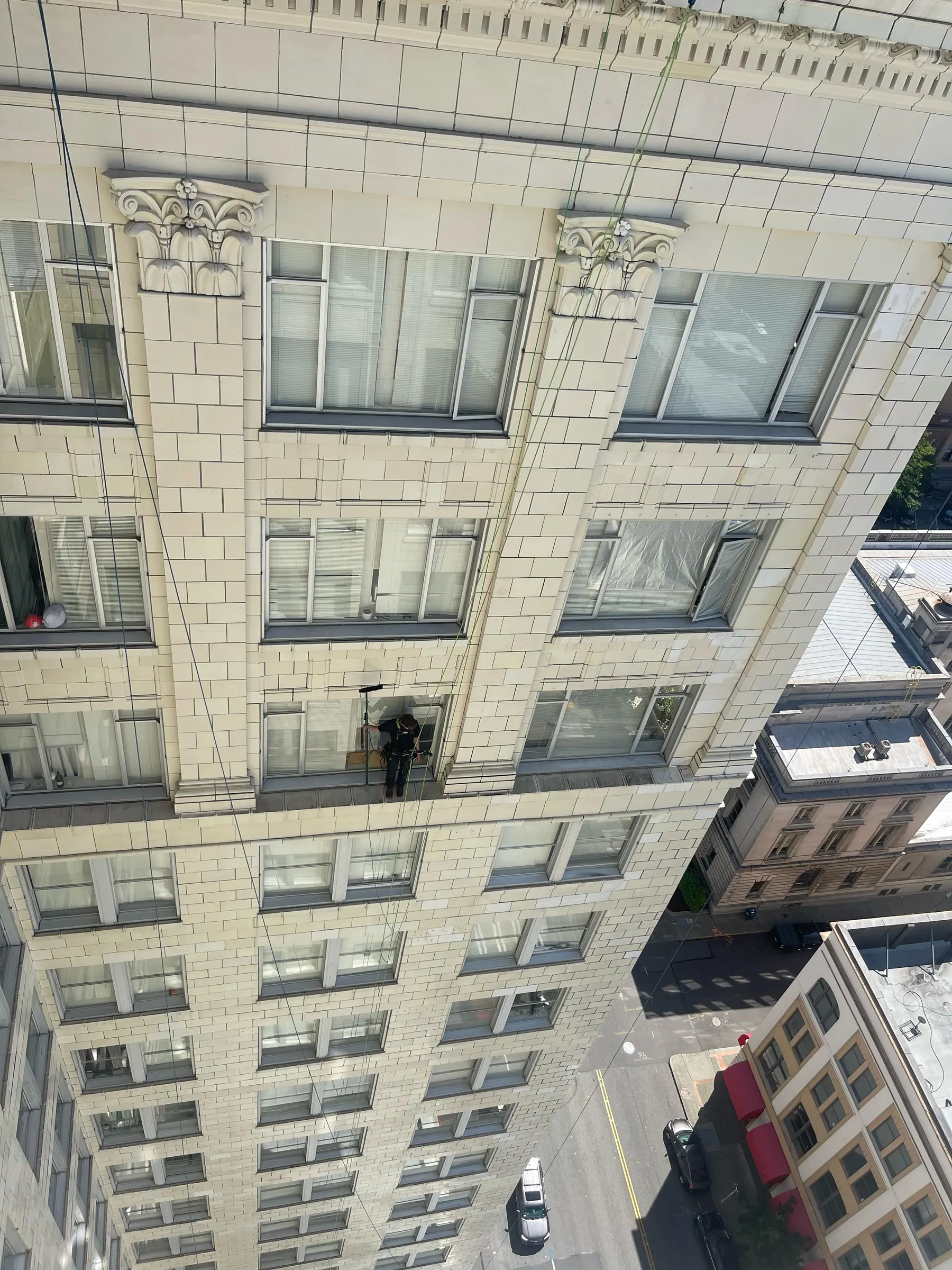Technician on ropes cleaning windows on a historic stone building, seen from above