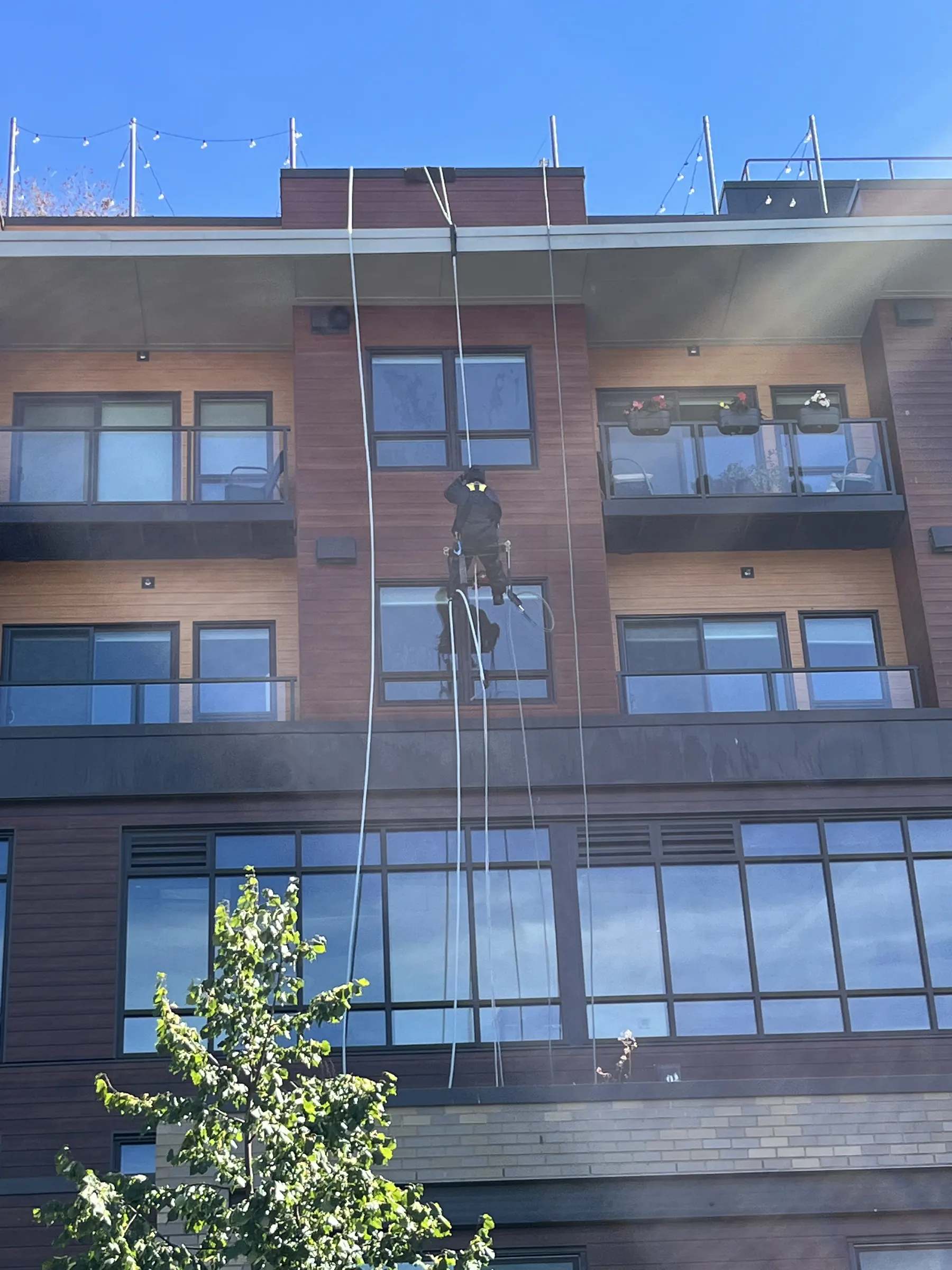 Technician descending the face of a mid-rise apartment building to clean windows