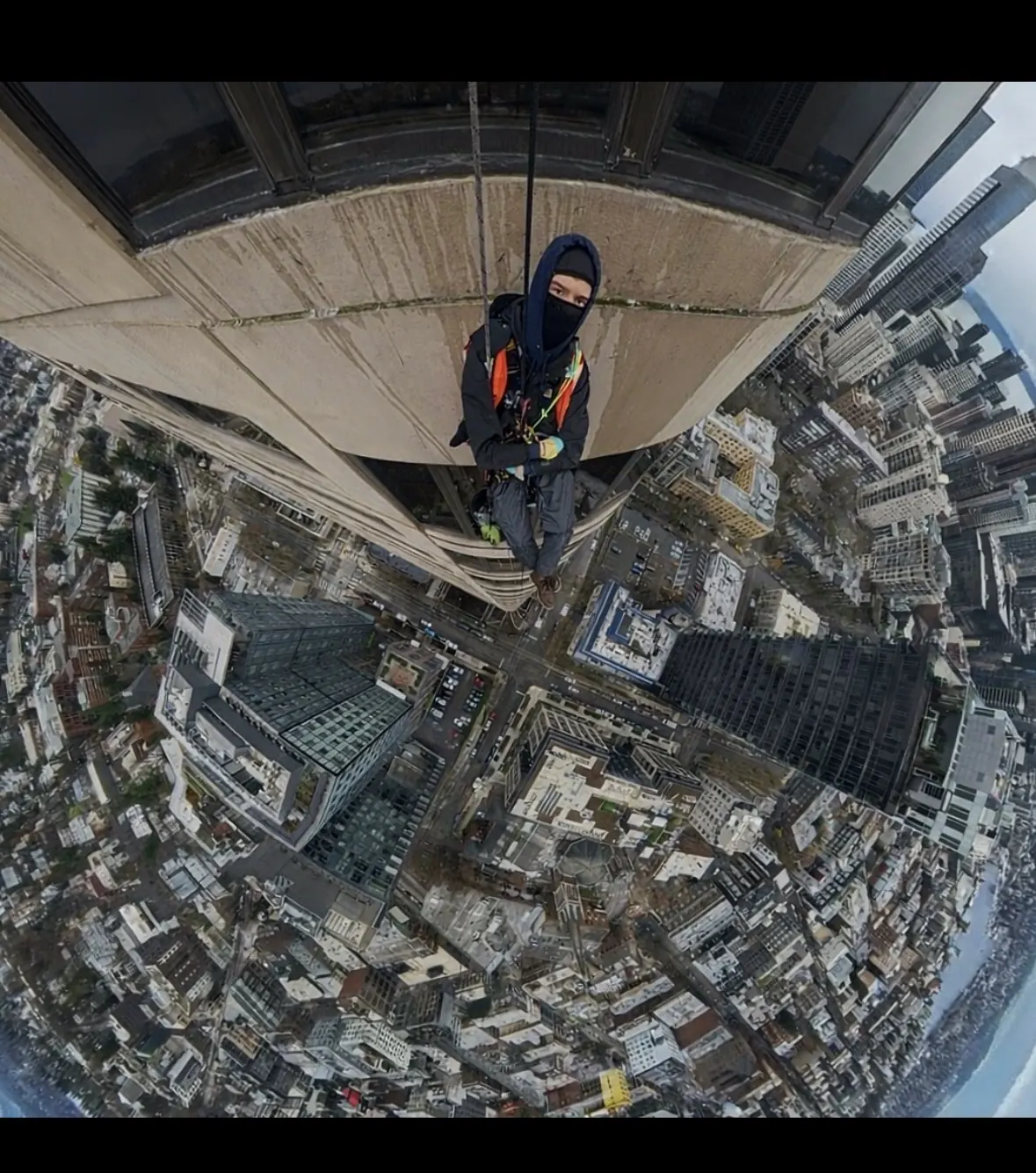 Technician hanging on ropes beneath a building overhang with the city far below