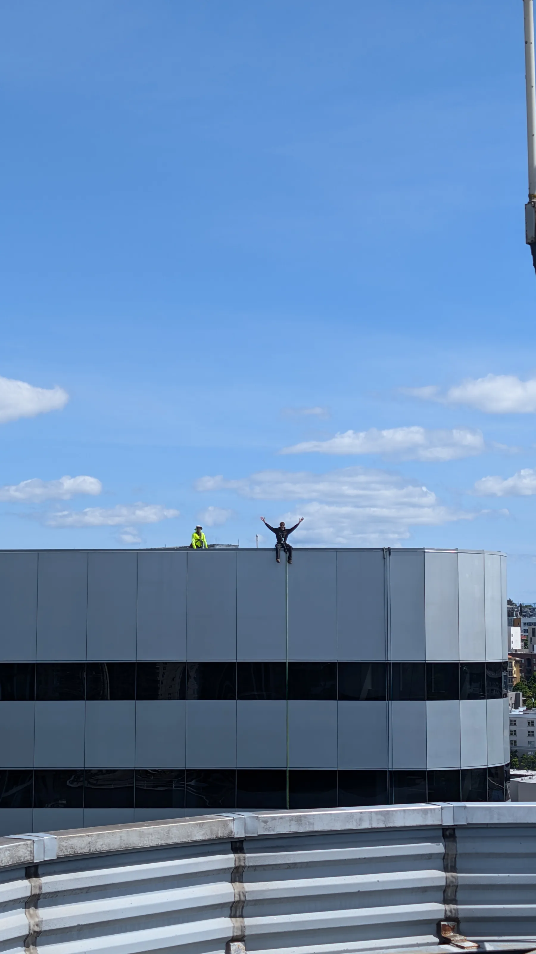 Technician standing at the edge of a rooftop with both arms raised against a blue sky