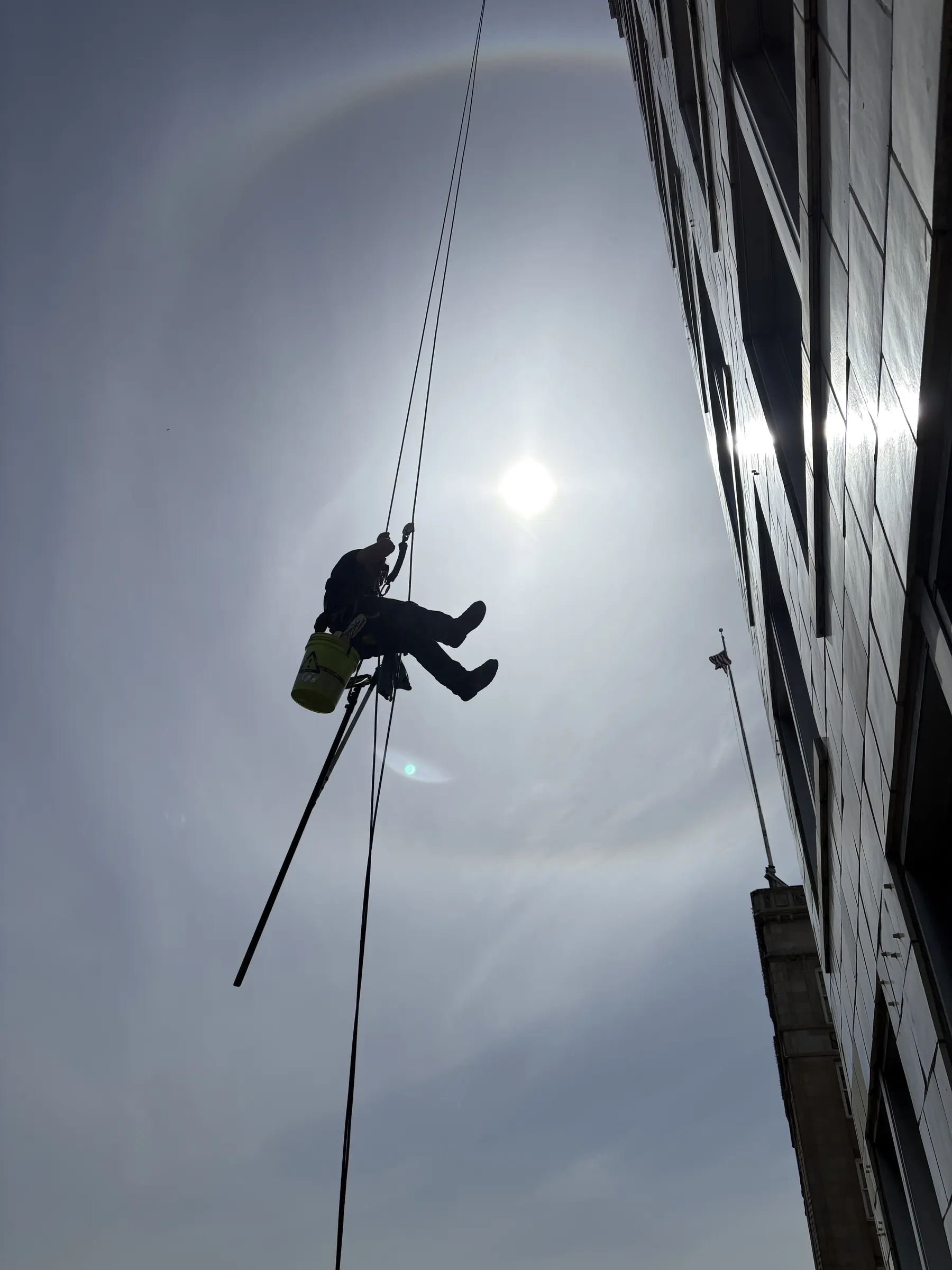 Rope access technician silhouetted against the sun beside an office building