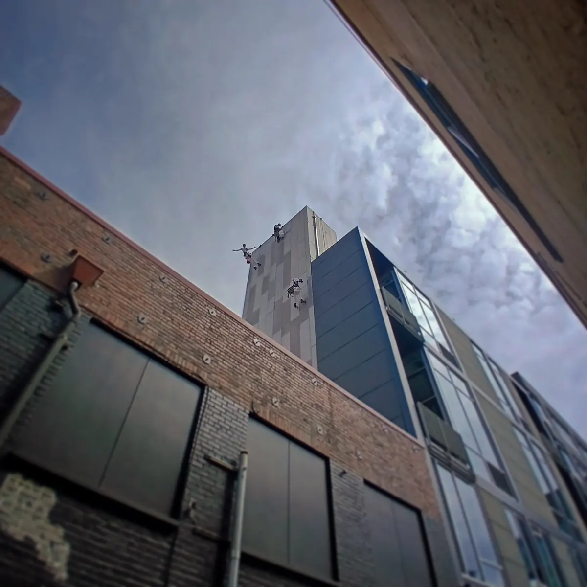 Looking up at technicians working near the top of a tower above a brick building